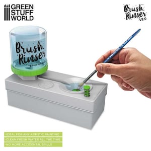 May include: A white plastic brush rinser with a clear plastic water reservoir. The reservoir has a green lid with the text "Brush Rinser" and "Green Stuff World". A hand is holding a blue paintbrush over the rinser's opening.