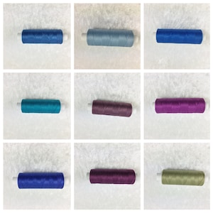 Könnte beinhalten: Neun Garnrollen in verschiedenen Farben, darunter Blau, Türkis, Lila und Grün. Die Rollen sind in drei Reihen zu je drei angeordnet.