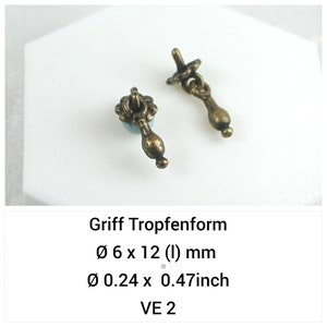 May include: Two antique brass-colored metal drop-shaped drawer pulls with a floral-shaped base. The text reads Griff Tropfenform, Ø 6 x 12 (l) mm, Ø 0.24 x 0.47inch, VE 2. Each pull features a rounded, teardrop-shaped handle attached to a circular base.