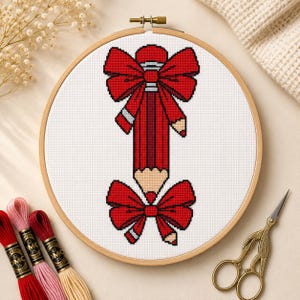 May include: A cross-stitch embroidery project in a round wooden hoop featuring a red pencil design adorned with two large red bows. The pencil is positioned vertically with a bow at the top and bottom, rendered in red, black, and tan thread on white fabric.