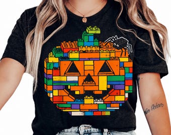 Puede incluir: Una camiseta de manga corta en color gris carbón oscuro con un gráfico grande de una calabaza de Halloween construida con bloques de construcción de plástico de colores. El diseño incluye una araña negra en la esquina superior derecha.