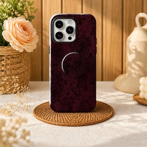 May include: A dark burgundy smartphone case featuring a subtle, repeating rose pattern across the entire back surface. The case includes a circular cutout for the camera module and a prominent, semi-circular pop-out grip attached to the center.