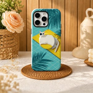 May include: A phone case featuring a graphic of a white cat wearing sunglasses while lounging on a yellow pool float. The background depicts a blue tiled swimming pool surface with dark palm leaf shadows cast across the scene.