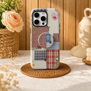 May include: A smartphone case featuring a patchwork design of red, blue, and white gingham, cable knit textures, and floral motifs. The case includes a circular pop-out grip, small ladybug illustrations, a heart, and a star graphic.