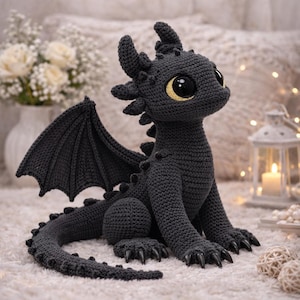 Könnte beinhalten: Ein dunkelgraues, gehäkeltes Drachen-Stofftier mit großen, glänzenden schwarzen Augen mit gelben Iris, spitzen Ohren, einem langen Schwanz und detaillierten Flügeln. Die Kreatur hat kleine Stacheln auf dem Rücken und scharfe, schwarze Krallen.