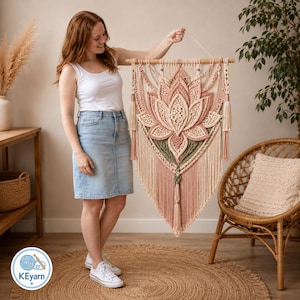 May include: A large macrame wall hanging featuring a central lotus flower design in shades of dusty rose, cream, and sage green. The piece is suspended from a wooden dowel and includes intricate knotted patterns, long fringe, and decorative tassels.