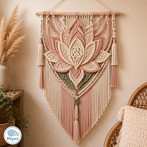 May include: A macrame wall hanging featuring a large central lotus flower design in cream, dusty pink, and sage green cotton cord. The piece is suspended from a horizontal wooden dowel and includes decorative side tassels and a long central tassel.