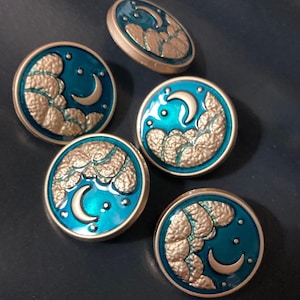 May include: Five circular buttons featuring a metallic gold crescent moon and textured clouds set against a vibrant teal enamel background. Each button has a raised gold rim and small gold dots representing stars scattered across the surface.