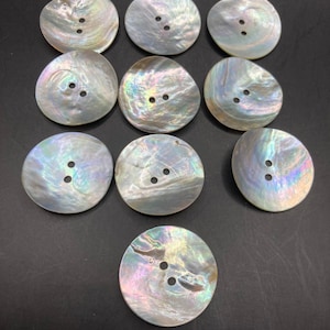 May include: Ten circular mother-of-pearl buttons arranged in a grid pattern. Each button features a smooth, iridescent surface with a natural pearlescent sheen displaying subtle shifts of pink, blue, and green. Every button has two central holes.
