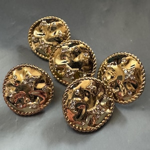 May include: A set of four circular gold-toned buttons featuring a raised celestial design with a crescent moon and stars. Each button has a twisted rope-style border and is accented with small, clear embedded crystals throughout the surface.