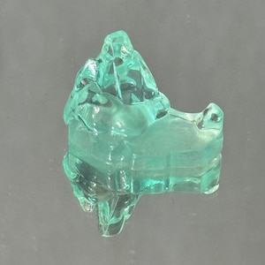 May include: A translucent, light green glass figurine shaped like a stylised mountain or rock formation. The object features smooth, rounded edges and a clear, polished surface that reflects light, creating a bright, glassy appearance throughout.