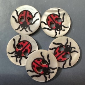 May include: Five round, off-white buttons, each featuring a two-hole design and a printed graphic of a red ladybird with black spots and black legs. The buttons have a smooth, slightly iridescent surface texture and are arranged in a cluster.