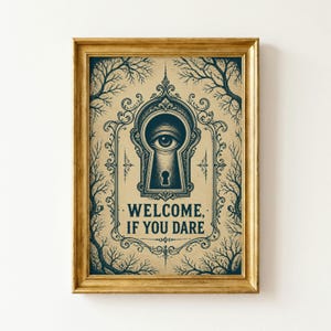May include: A framed print featuring a dark blue illustration on a tan background. The design shows a central keyhole containing a single eye, surrounded by ornate scrollwork and bare tree branches. The text reads: WELCOME, IF YOU DARE.