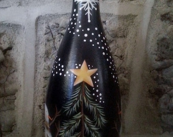 May include: A black glass bottle with a white snowflake and white dots painted on it. A green pine tree with a yellow star is painted on the bottle. The bottle is decorated with white snow at the bottom.