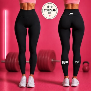Könnte beinhalten: Hoch taillierte schwarze Leggings mit einem weißen Maus-Symbol am hinteren Bund und dem in Weiß auf die Unterschenkel gedruckten Text gym rat. Die Leggings sind von vorne und hinten zu sehen und mit weißen Sportschuhen kombiniert.