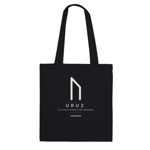 Könnte beinhalten: Eine schwarze Tragetasche mit einer weißen Uruz-Runengrafik in der Mitte auf der Vorderseite. Unter der Rune steht der Text URUZ, THE RUNE OF STRENGTH AND ENDURANCE, und nordstoke. Die Tasche hat zwei lange Schulterriemen und eine rechteckige Form.
