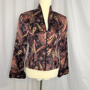 May include: A black long-sleeve jacket featuring a vibrant multi-colored paisley pattern in shades of pink, yellow, and green. The jacket has a high collar, a front button closure with small black buttons, and cuffs with black trim detailing.