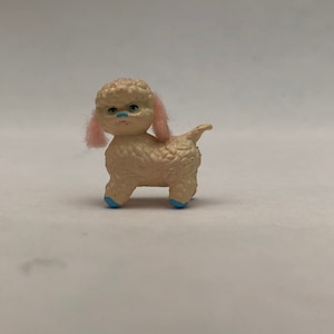 May include: A small, white, fluffy toy poodle with pink ears and blue feet. The toy is made of plastic and has a realistic appearance.