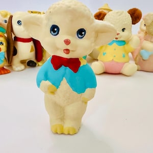 May include: A collection of vintage rubber toys, including a lamb wearing a blue shirt and red bow tie, a chick, a dog, and two puppies. The toys are all white with colorful accents.