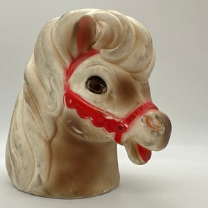 Op de afbeelding: Een wit en bruin keramiek paardenhoofd met een rood hoofdstel. Het paard heeft een witte manen en staart. De ogen van het paard zijn bruin en de mond is open.