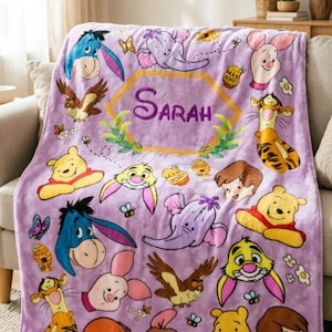 Puede incluir: Una manta de forro polar de color morado claro con un patrón repetitivo de personajes de Winnie the Pooh, incluyendo a Igor, Piglet, Tigger, Rabbit y Búho. El centro muestra un marco hexagonal amarillo con el nombre Sarah en morado.