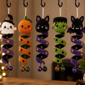 May include: Five hanging crochet ornaments featuring a ghost, pumpkin, black cat, Frankenstein monster, and bat. Each figure has a long, spiraling tail decorated with small stars and two metallic jingle bells at the bottom, suspended by white strings.