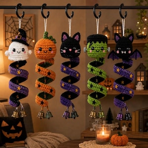 Może przedstawiać: Pięć szydełkowych ozdób wiszących na Halloween przedstawiających ducha, dynię, czarnego kota, potwora Frankensteina i nietoperza. Każda figurka ma długi, spiralny ogon ozdobiony małymi żółtymi gwiazdkami i dwoma metalowymi dzwoneczkami.