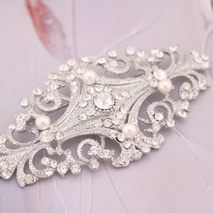 May include: A silver filigree brooch with a diamond-shaped center and four faux pearl accents.