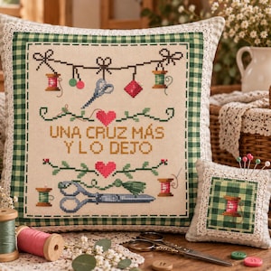 Puede incluir: Un cojín cuadrado con un diseño de punto de cruz de artículos de costura y el texto "UNA CRUZ MÁS Y LO DEJO" en naranja, flanqueado por dos corazones rosas, con un borde de cuadros vichy verdes y encaje blanco, junto a un alfiletero pequeño a juego.