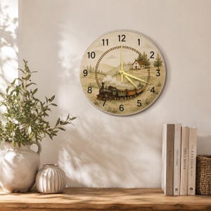 May include: A round wall clock featuring a vintage steam train illustration on a rural landscape background with a house, trees, and hills. The clock face has black Arabic numerals and thin gold-colored hands indicating the time.