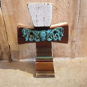 May include: A wooden cross with a distressed white top and a turquoise floral design. The cross is made of reclaimed wood and has a rustic look.