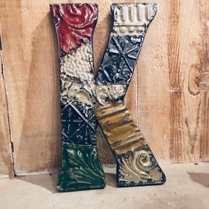 May include: A decorative metal letter "K" with a patchwork design. The letter is composed of various textured metal pieces in red, white, green, yellow, and black. The letter is approximately 10 inches tall.