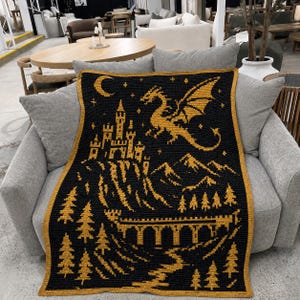 May include: A rectangular crochet blanket featuring a black background with a gold-colored pattern. The design depicts a castle on a hill, a flying dragon, a crescent moon, stars, a stone bridge, a winding path, and several pine trees.