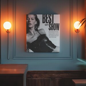 May include: A square black and white wall art print featuring a portrait of a person wearing a dark top. The text BEST OF SHOW is printed in large bold letters at the top right, followed by smaller text describing fashion trends.
