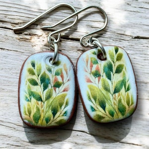 May include: A pair of silver dangle earrings with rectangular ceramic charms featuring a green and orange floral design.