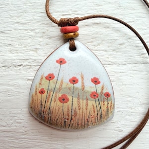 May include: A handmade pendant necklace featuring a painted poppy field design. The pendant is a white, triangular shape with a brown cord. The poppy flowers are red, and the field is a mix of yellow and brown.