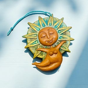 以下が含まれることがあります： 笑顔で腕を広げた太陽の形をした装飾品。太陽は茶色の顔、金とターコイズのハロー、茶色の体を持っています。吊り下げ用のターコイズの紐が付いています。