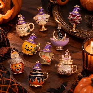 Può includere: Una collezione di nove ciondoli in metallo a tema Halloween con vari design, tra cui una tazza mummia, una zucca, un gatto nero su una mezzaluna, un castello e un gufo, tutti decorati con cappelli da strega viola e dettagli in smalto.