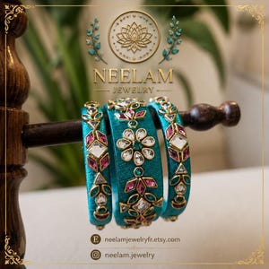 Può includere: Tre bracciali rigidi avvolti in seta color verde acqua con montature in metallo dorato e pietre trasparenti e rosa. Il bracciale centrale presenta un motivo floreale, mentre i due esterni mostrano motivi geometrici.
