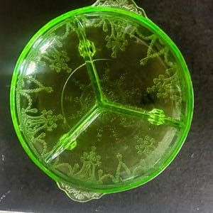 May include: A round, vibrant lime green glass serving dish featuring three internal compartments separated by raised glass dividers. The surface is decorated with an intricate, embossed pattern of repeating floral and architectural motifs.
