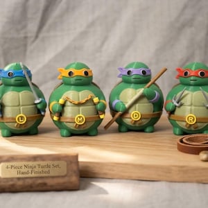 May include: A set of four green turtle figurines with round bodies, each wearing a coloured mask and a brown belt with a circular buckle featuring the letters L, M, D, or R. They hold miniature weapons including swords, nunchucks, a staff, and sai.