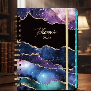 May include: A 2027 spiral-bound planner featuring a galaxy-inspired cover with layers of purple, blue, and teal hues accented by gold glitter edges. The cover displays the text Planner 2027 in gold script. It includes a gold elastic closure band.