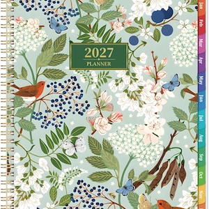 May include: A 2027 planner with a light green cover featuring a botanical illustration of white flowers, dark blue berries, brown birds, and various butterflies. The planner has a gold-colored spiral binding on the left and monthly tabbed dividers.