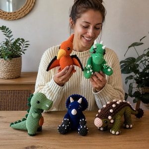 Puede incluir: Una colección de cinco juguetes de dinosaurios hechos a mano en ganchillo. El conjunto incluye un pterodáctilo naranja, un triceratops verde, un dinosaurio verde claro de pie, un triceratops azul oscuro y un anquilosaurio marrón y verde.