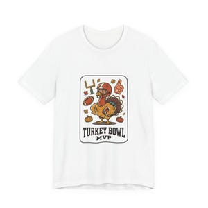 May include: A white short-sleeve t-shirt featuring a graphic of a turkey wearing a football helmet, holding a football, and surrounded by a goalpost, a foam finger, pumpkins, and autumn leaves, with the text Turkey Bowl MVP printed below.