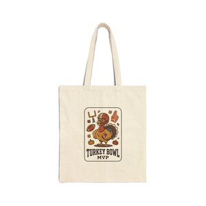 May include: A natural-colored canvas tote bag featuring a central graphic of a cartoon turkey wearing a football helmet and holding a football. The design includes a goalpost, a foam finger, and pumpkins, with the text "TURKEY BOWL MVP" below.