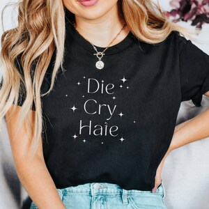 May include: Black t-shirt with white text that reads "Die Cry Haie" with white stars around the text.
