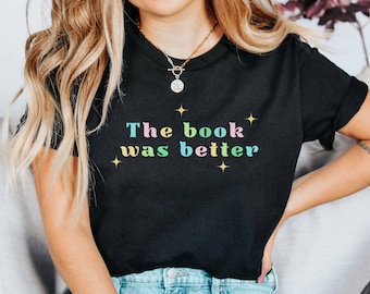 May include: A black t-shirt with the text "The book was better" in rainbow colors. The text is surrounded by small yellow stars.