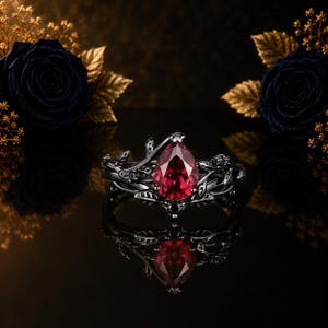 Puede incluir: Un anillo de metal negro con una piedra preciosa roja en forma de pera en el centro. La banda presenta motivos intrincados de enredaderas y hojas que envuelven la piedra central, acentuados por pequeñas piedras negras incrustadas.