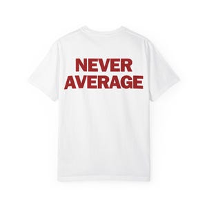 Può includere: Una t-shirt bianca a maniche corte con la scritta NEVER AVERAGE stampata in grassetto e in lettere maiuscole rosso scuro al centro della schiena. Il capo presenta un girocollo e una vestibilità standard, con un design semplice e pulito.